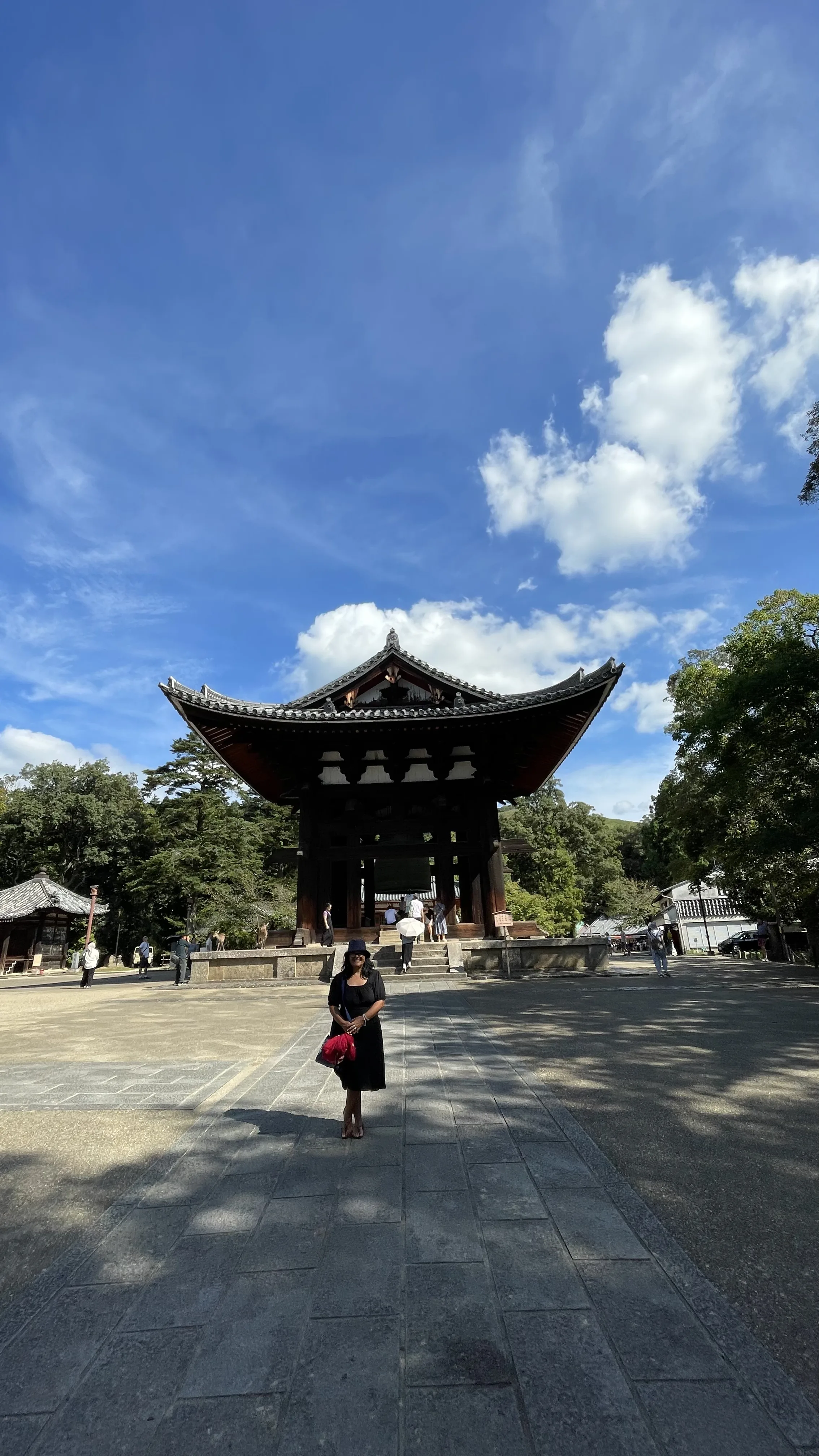 Mulher na frente pequeno templo tradicional de madeira com sino e com telhado de telhas cinzentas cercado por árvores no Japão.
