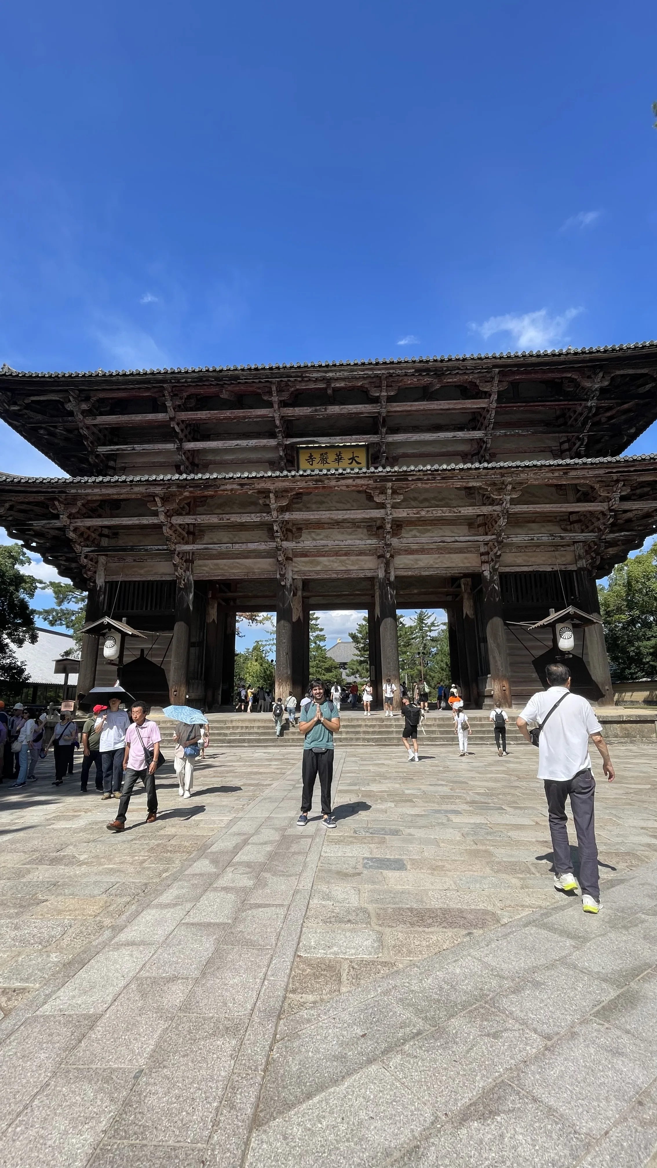 Homem de pé com as mãos em prece na praça pavimentada em frente à grandiosa fachada de madeira do Portão Nandaimon no Templo Todai-ji em Nara no Japão.