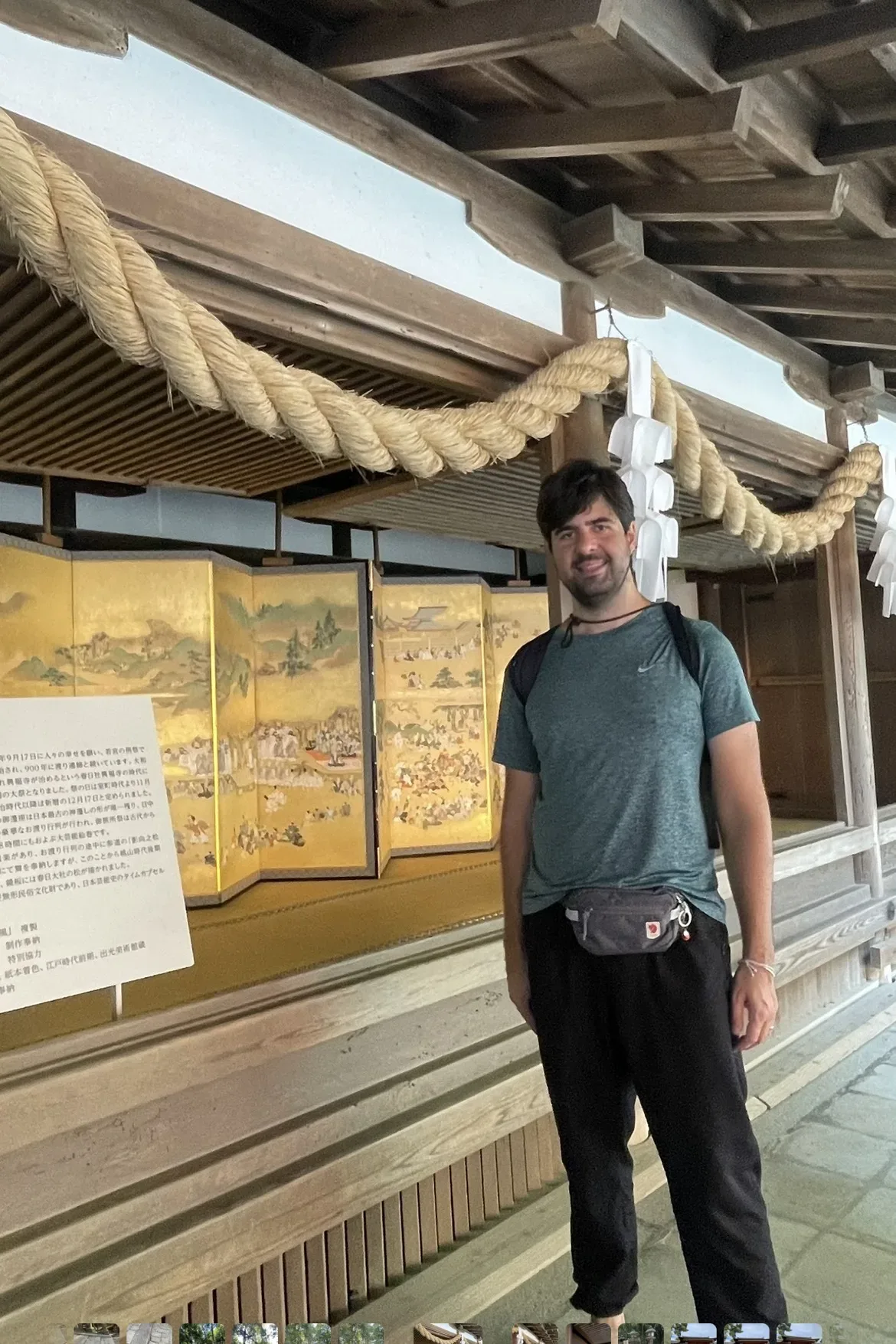 Turista posa ao lado de biombo dourado sob corda shimenawa no pavilhão Naorai-den do Santuário Kasuga Taisha em Nara, Japão.