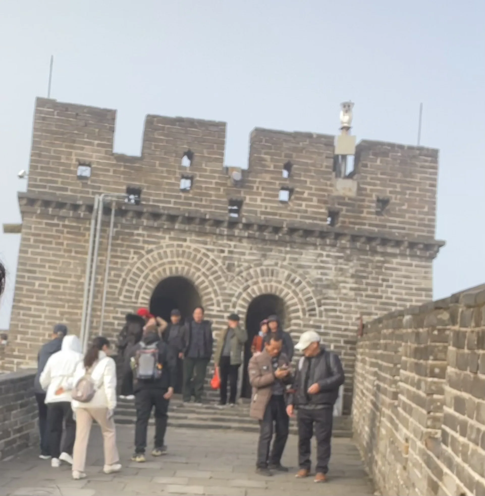 Visitantes caminhando pela imponente torre de vigia com arcos e ameias de tijolos antigos na famosa Muralha da China, registrando os detalhes arquitetônicos.