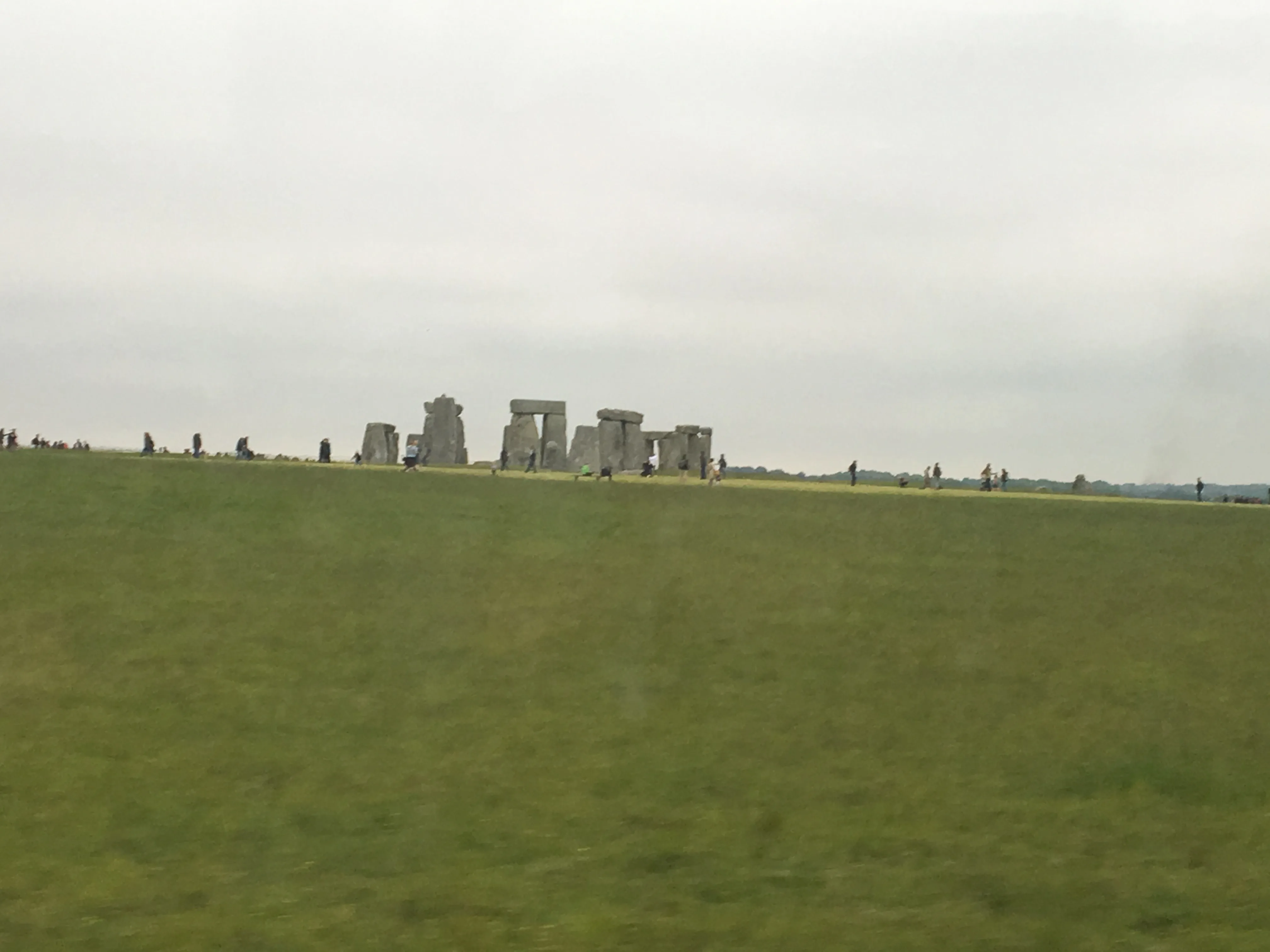 Monumento de pedras de Stonehenge na Inglaterra com grupo de visitantes ao fundo pelo caminho do campo.