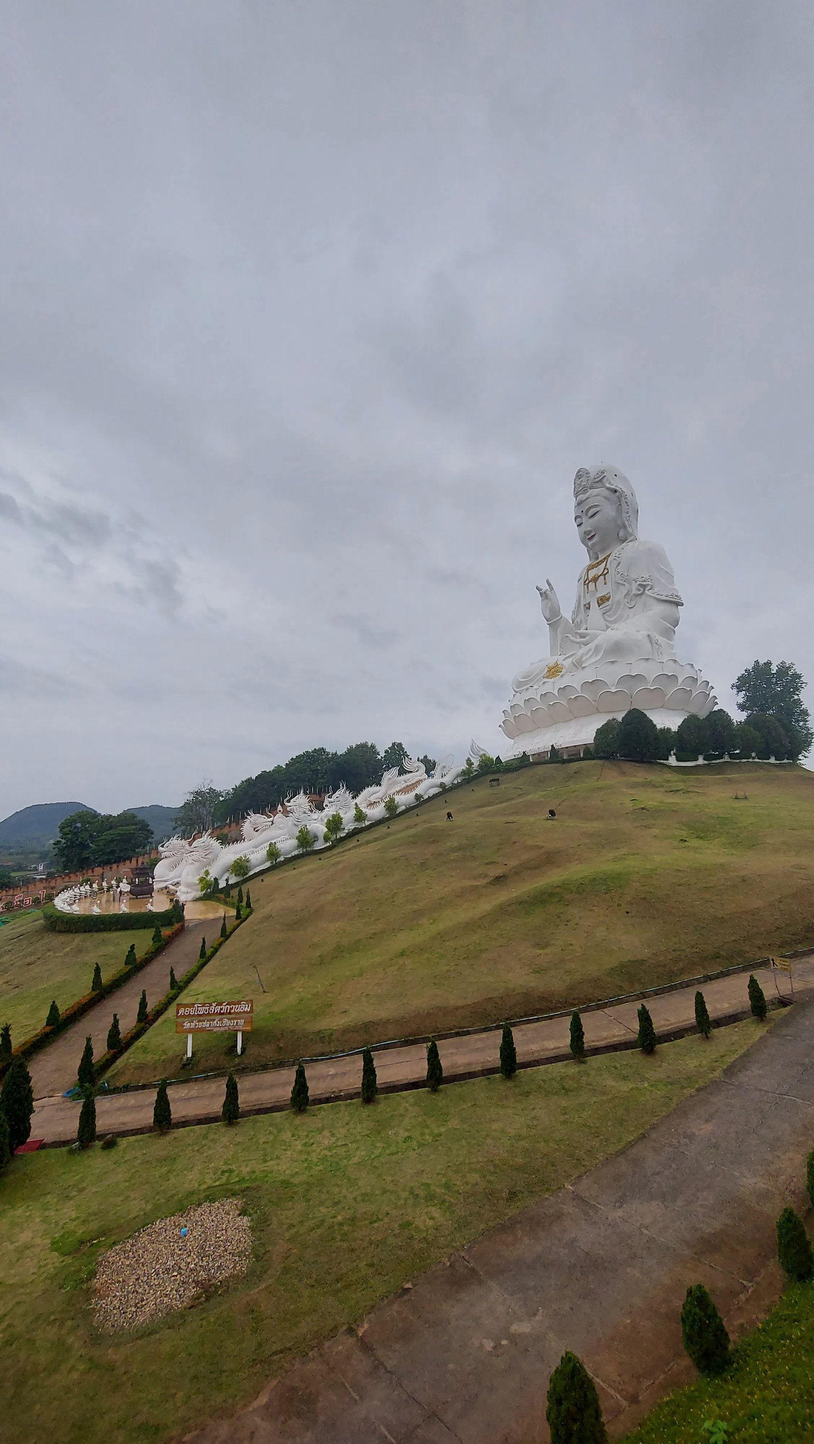 Vista panorâmica da imponente estátua branca gigante de Guanyin sentada sobre uma flor de lótus em uma encosta verde em Chiang Rai.