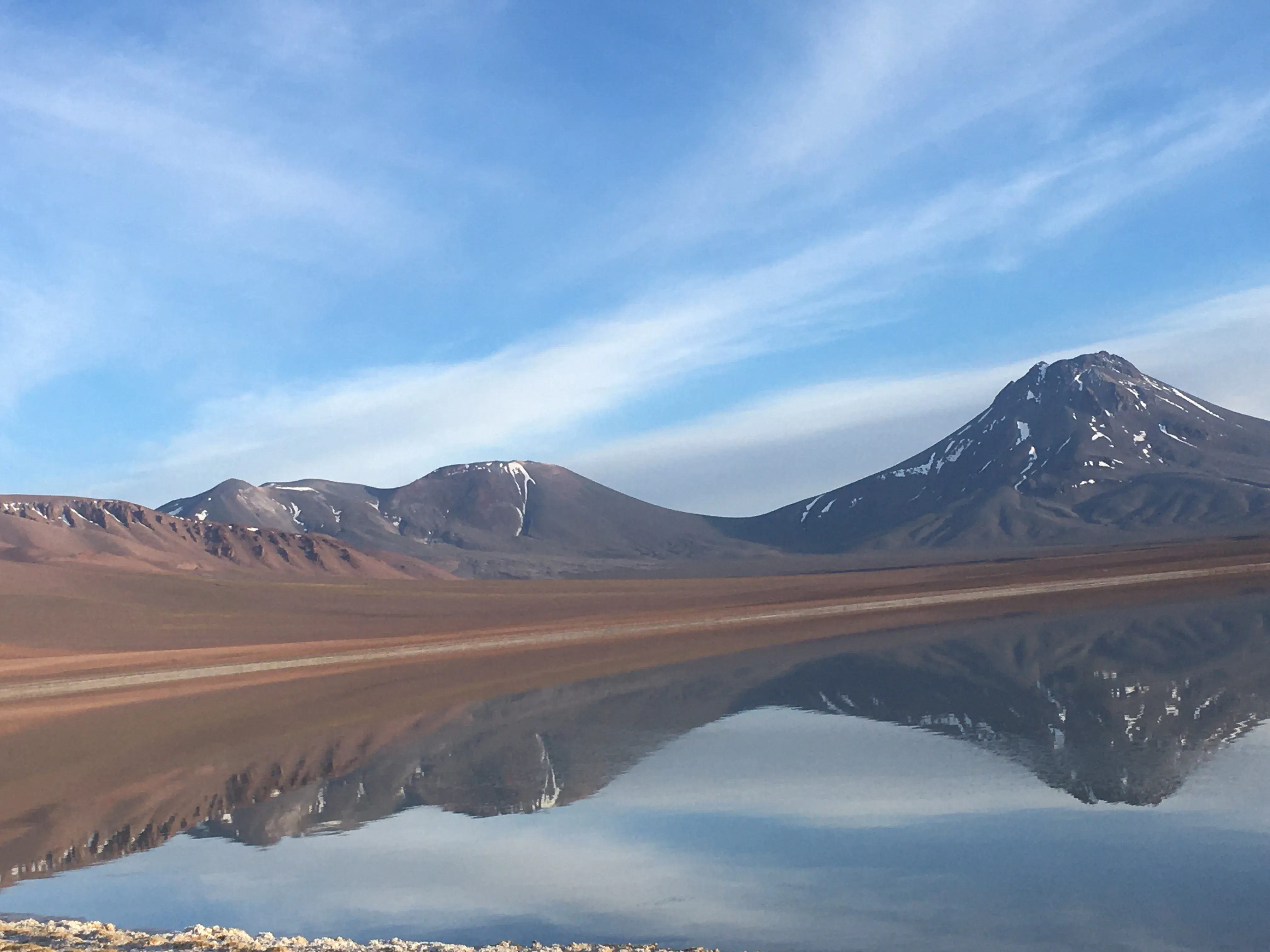 Reflexo de montanhas e do vulcão com neve no topo na superfície espelhada da Laguna Lejía, no Deserto do Atacama.