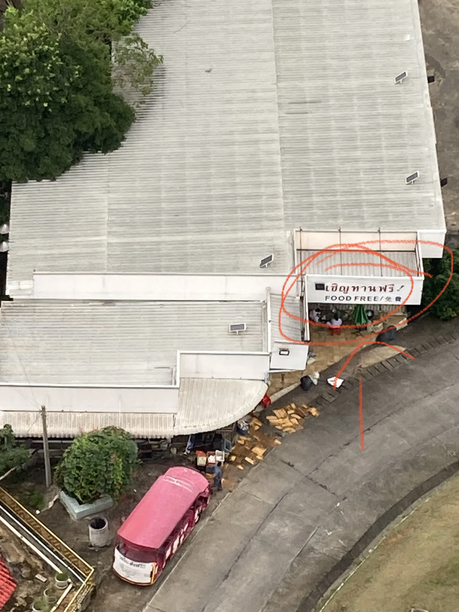 Vista aérea detalhada de um edifício com placa indicando distribuição de comida gratuita ("Food Free"), com um veículo vermelho estacionado ao lado na área do templo em Chiang Rai