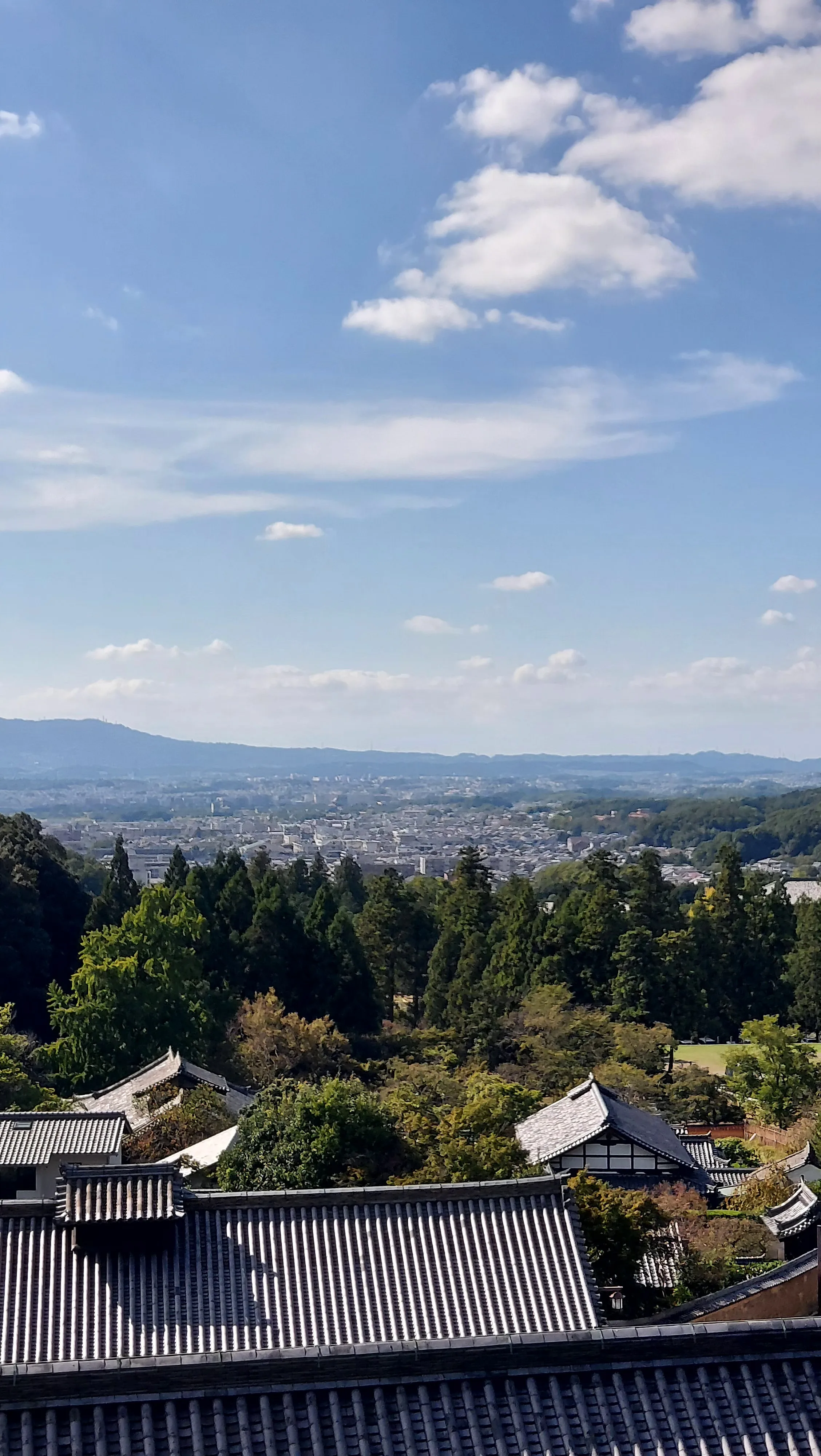 Vista panorâmica de Nara a partir do terraço de madeira do pavilhão Nigatsu-do, mostrando os tradicionais telhados do Templo Todaiji sob um céu azul ensolarado no Japão.