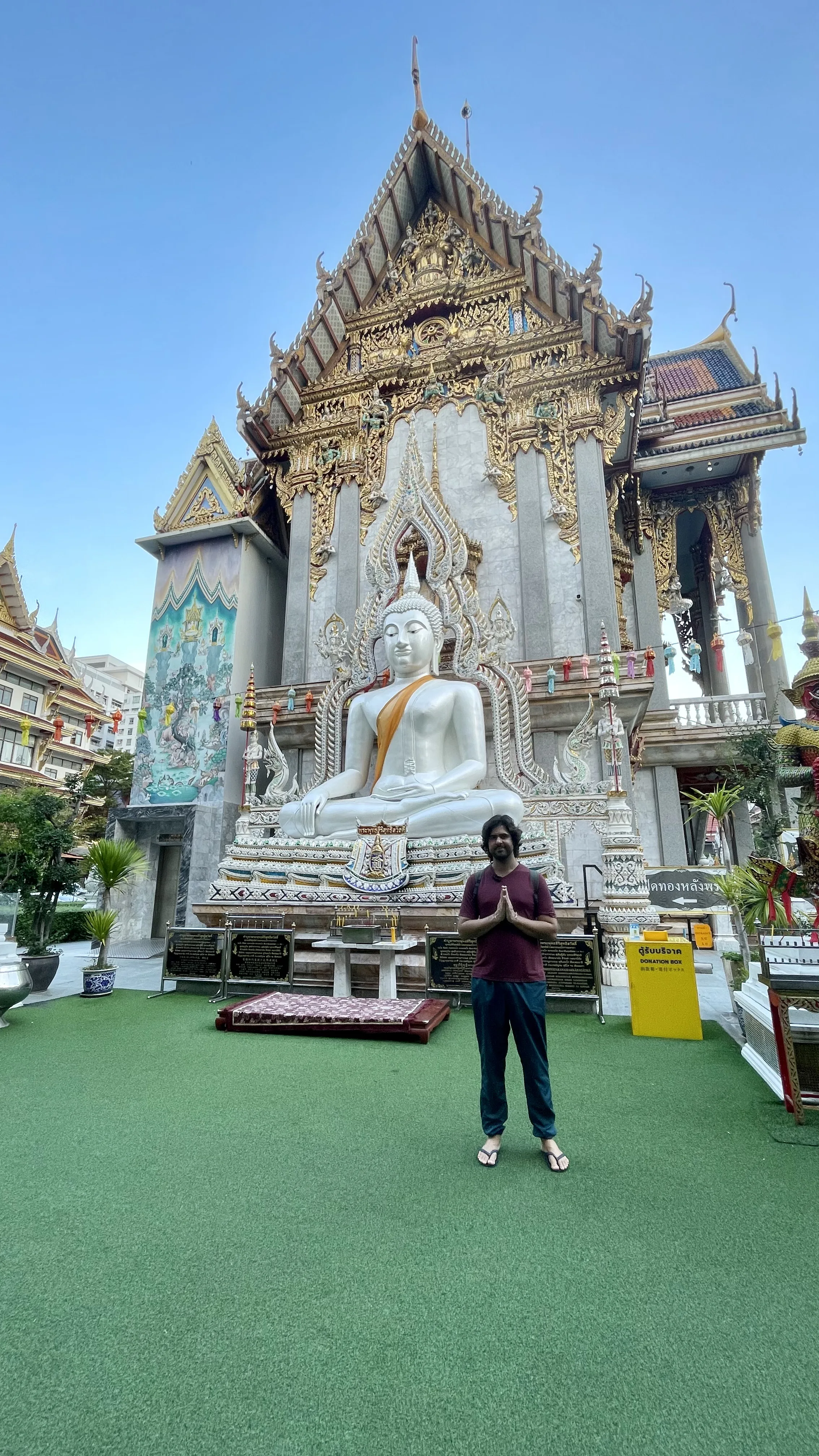 Um homem em pé com as mãos juntas em oração em frente à grande estátua de Buda branca e dourada no Wat Suthiwaram  em Banguecoque