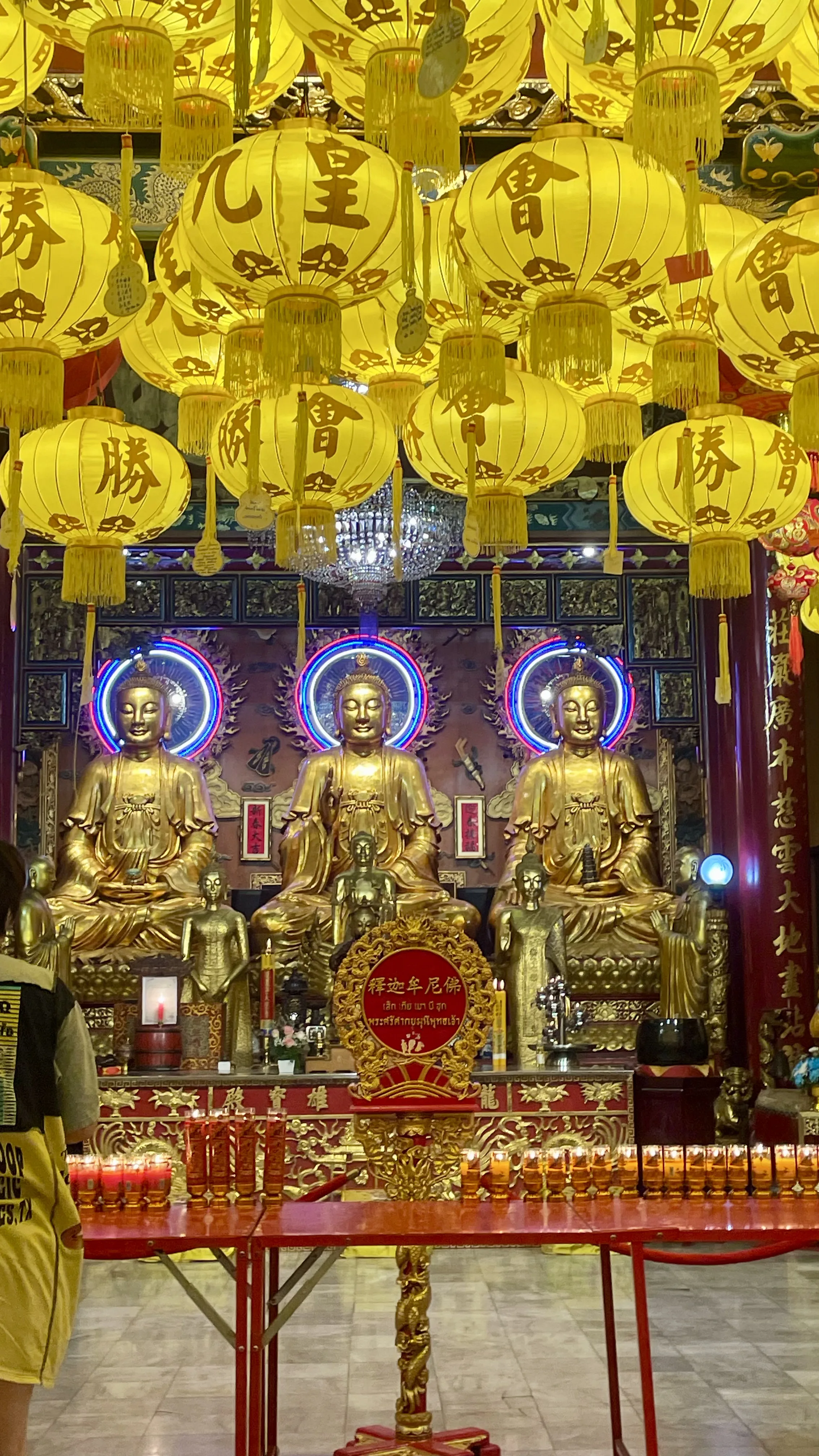 Altar ricamente decorado com três grandes estátuas douradas de Buda e lanternas amarelas suspensas no teto do Templo Chinês Wat Mangkon Kamalawat, em Banguecoque