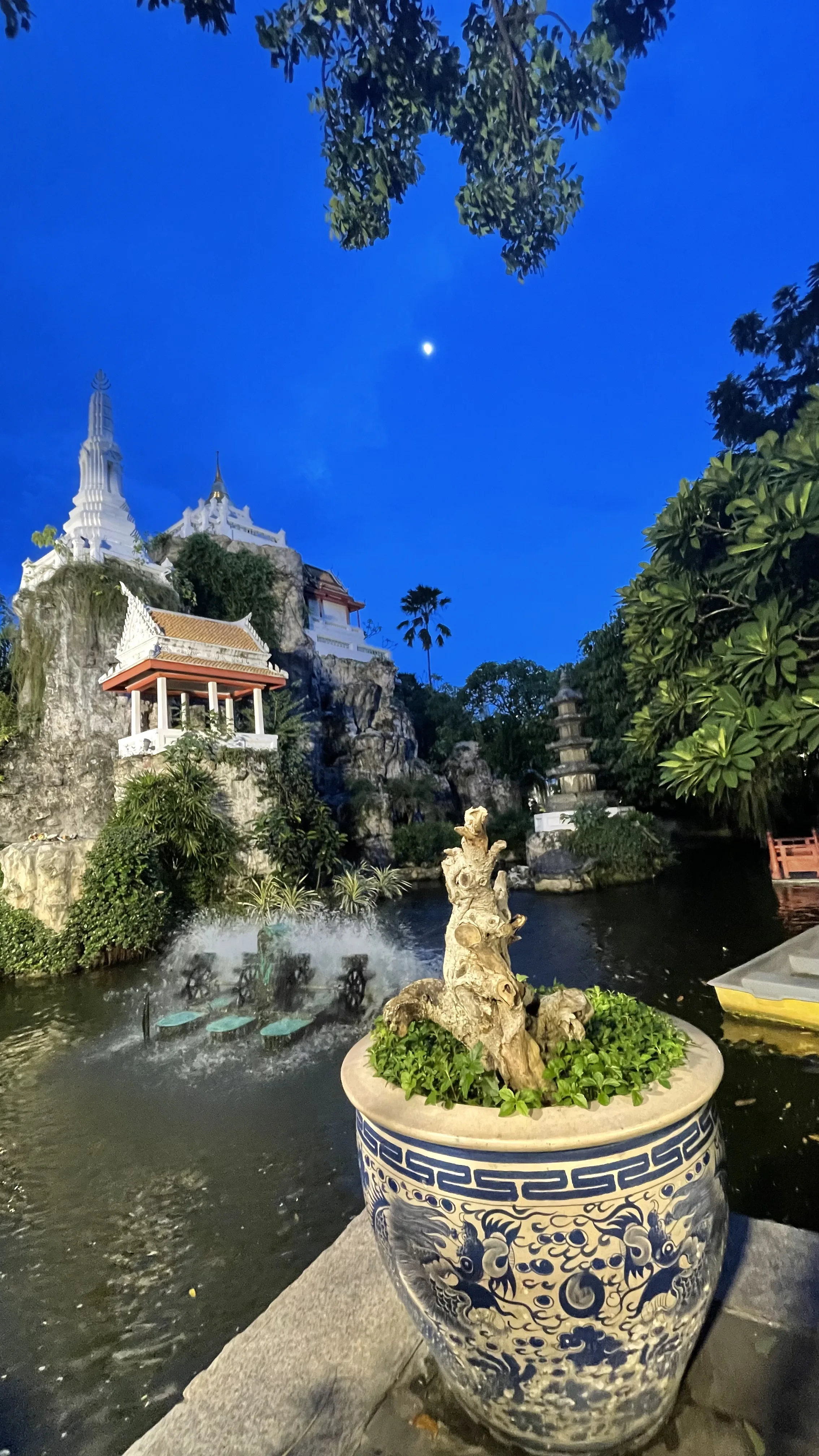 Jardim com lago, fonte e stupa branca no complexo do Wat Prayoon à noite em Banguecoque