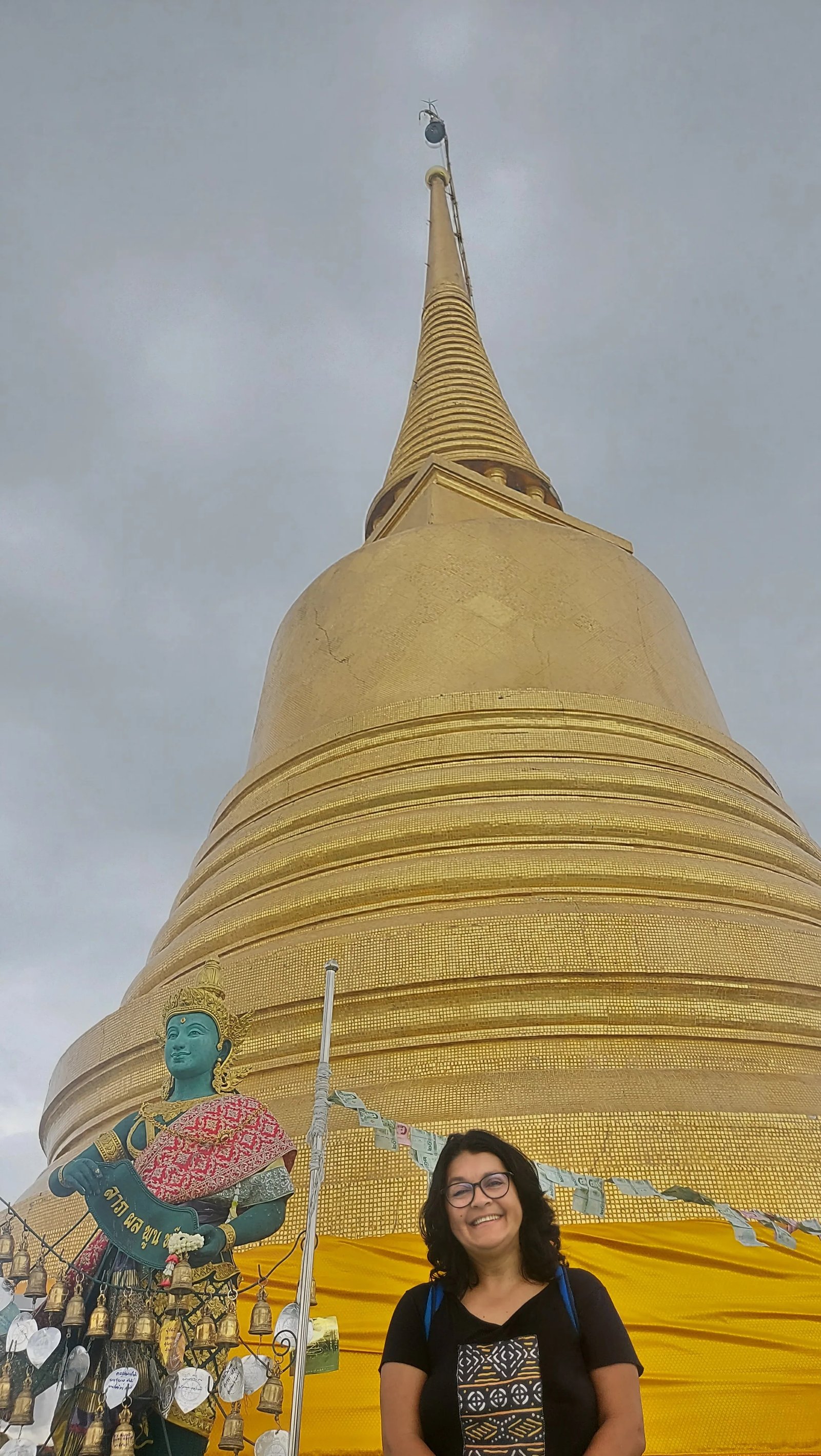 Mulher sorridente ao lado da imensa stupa dourada do Monte Dourado no Wat Saket em Banguecoque.