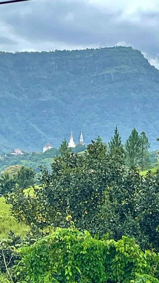 Vista de longe do templo Wat Phra That Pha Sorn Kaew com muito verde, as construções aparecem no fundo com a montanha atrás